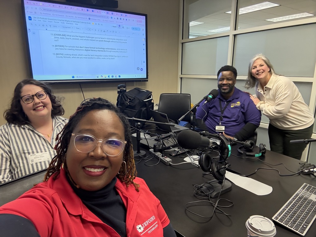 JEFCOED employees Charlsie Wigley and Delfreda Coleman sit at a table with a man and a woman and smile for a photo. Podcast equipment sits between them.