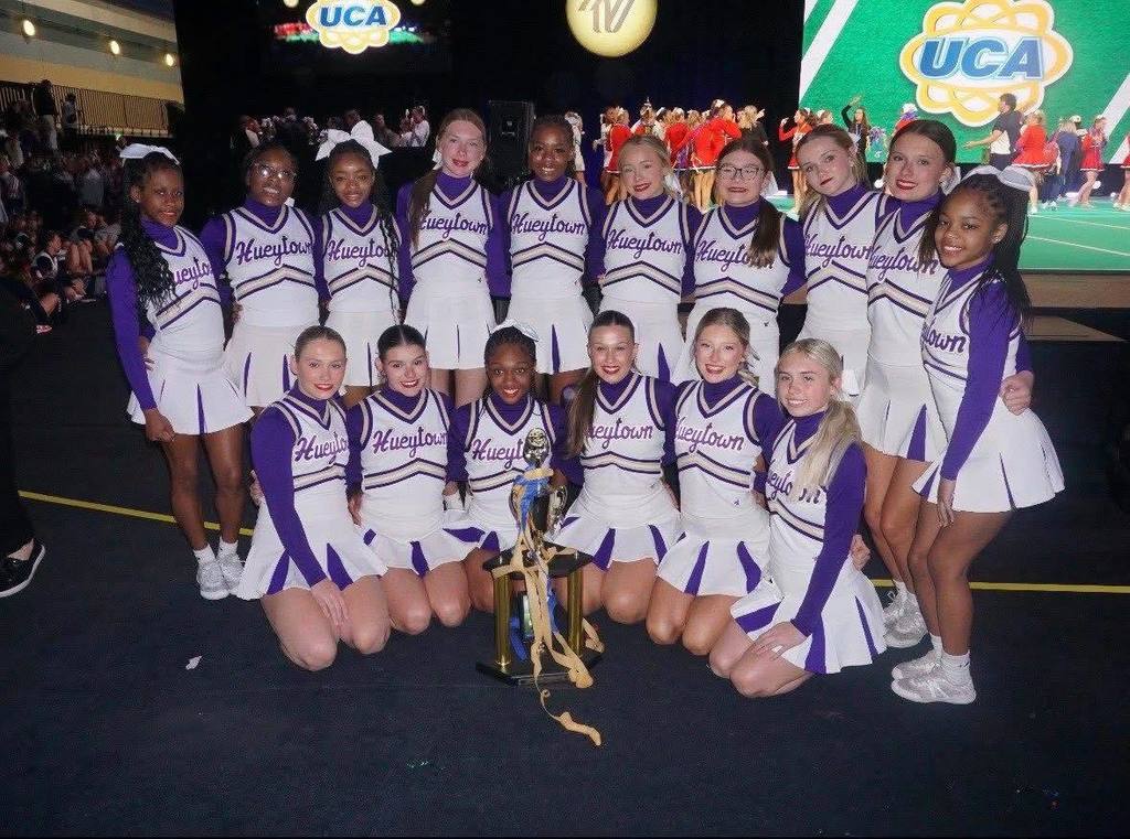 Hueytown High School cheerleaders wear their cheer uniforms and pose for a photo with a trophy.