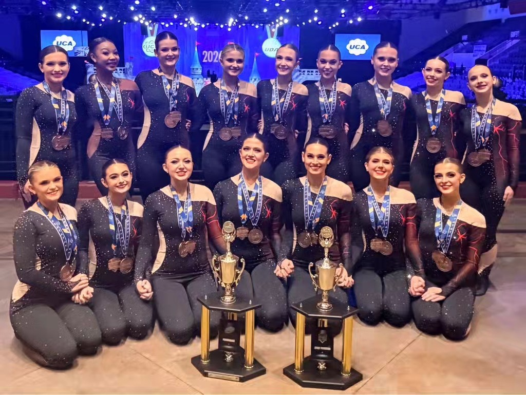 Gardendale High School's dance team poses for a photo in their competition uniforms when two trophies in front of them. Each of the members wears a medal.