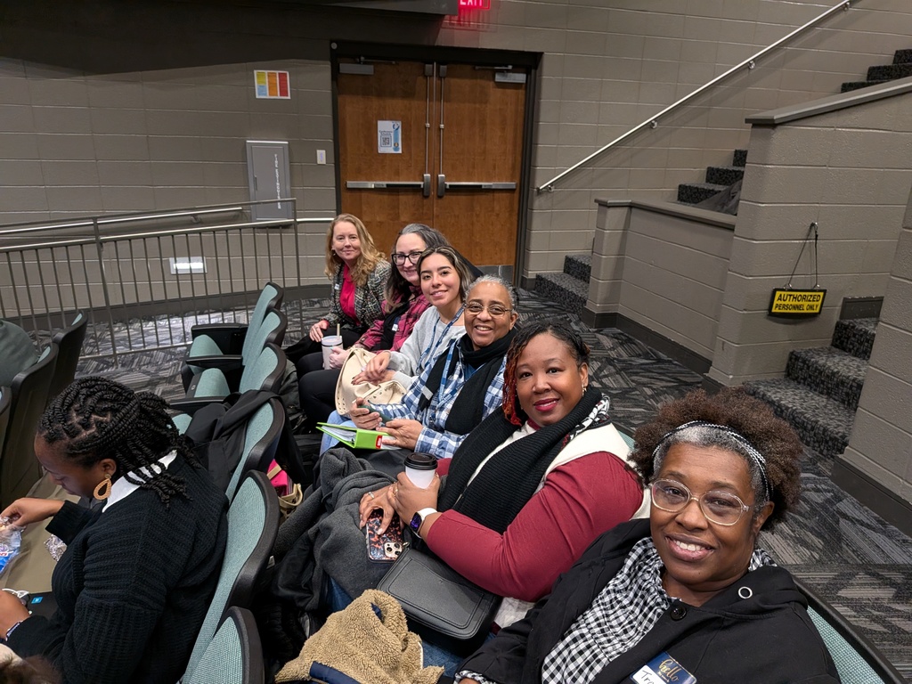 A group of women sit in auditorium chairs and smile for a photo.