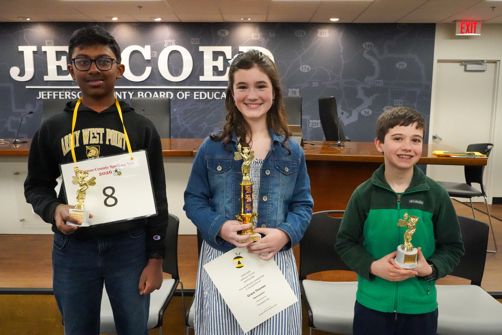The 1st, 2nd, and 3rd place winners of the Jefferson County spelling bee stand together for a photo inside the Jefferson County Schools board room. Each of the students hold a trophy in their hands.