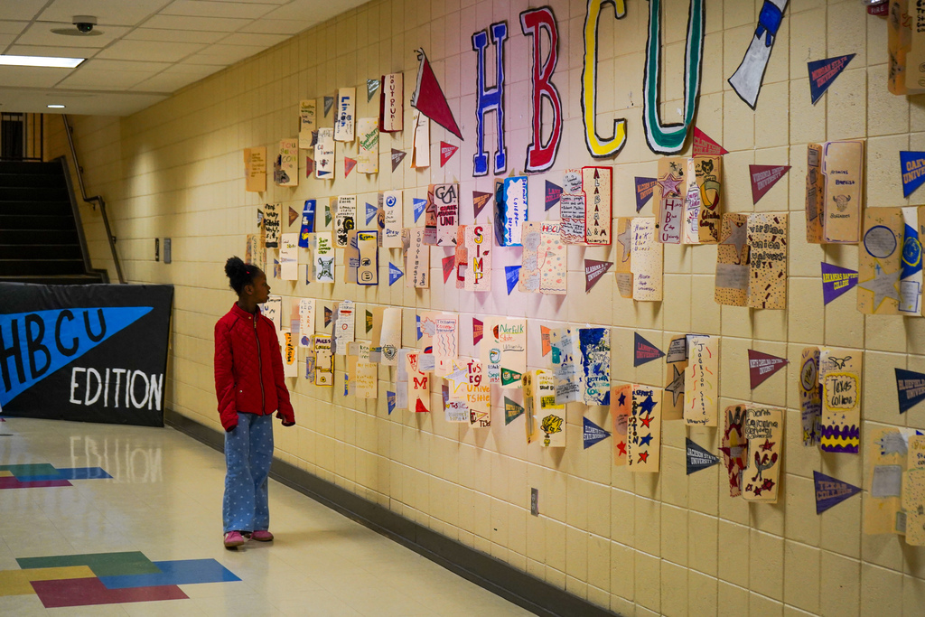 A little girl stands in a school hallway and looks at a wall featuring projects on HBCUs.