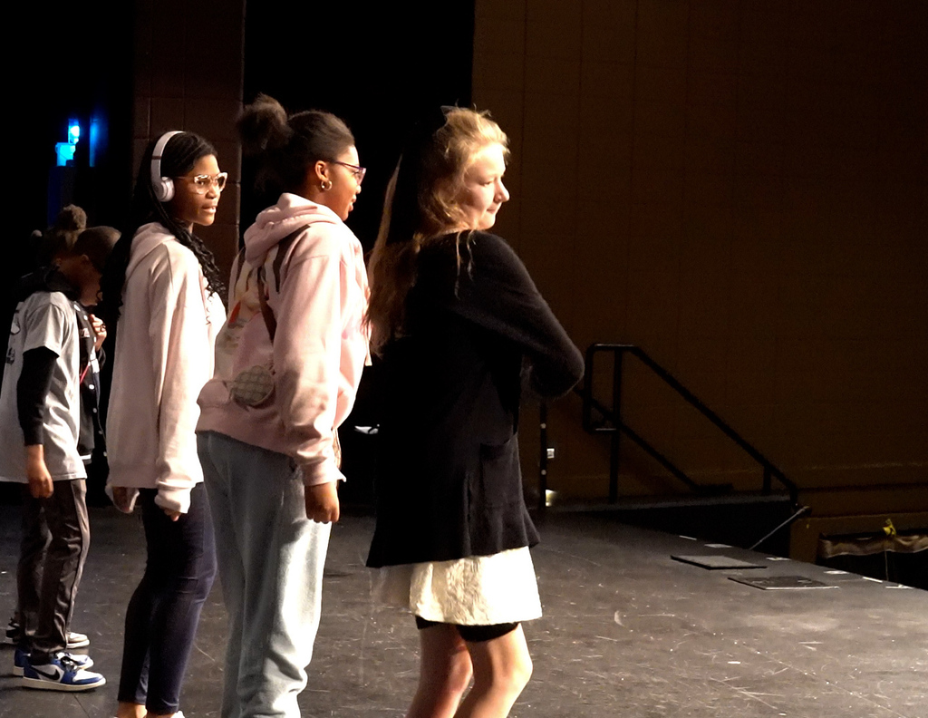 Four students perform a dance routine on a stage in an auditorium.