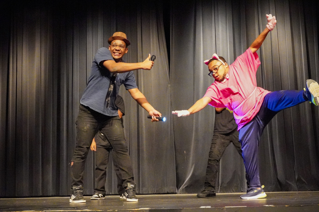 Two students dance on a stage. One is dressed like an investigator and the other is dressed like the Pink Panther. Two  other students dance  behind them in the background.