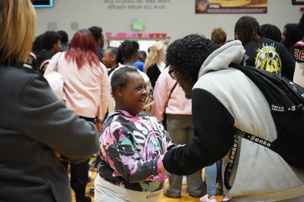 An adult and a student hold hands and smile while at a school dance.