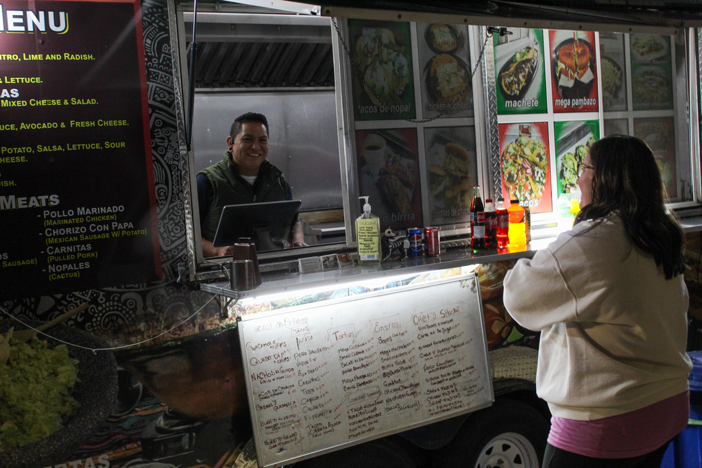 A man working at a food truck smiles as a woman gets ready to order.