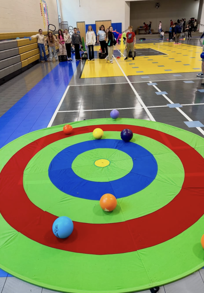 Students recreate the sport of curling in a school gym. They roll balls onto a target.