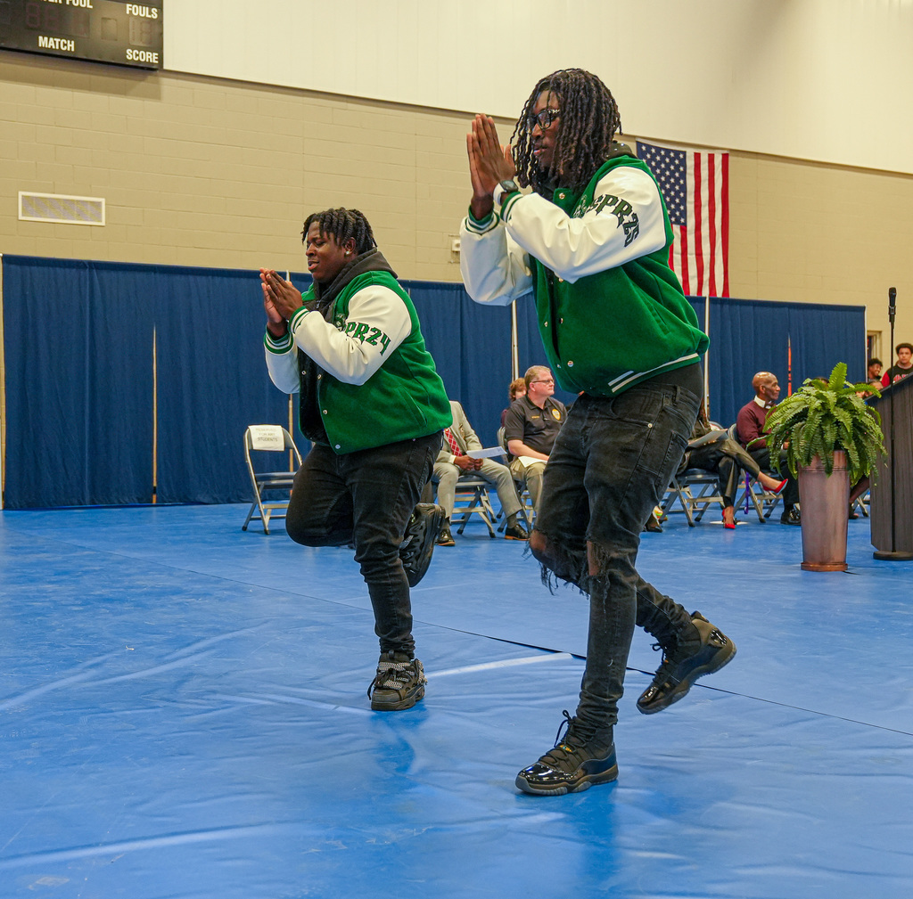 Two people wear matching green jackets and black pants and perform a routine.