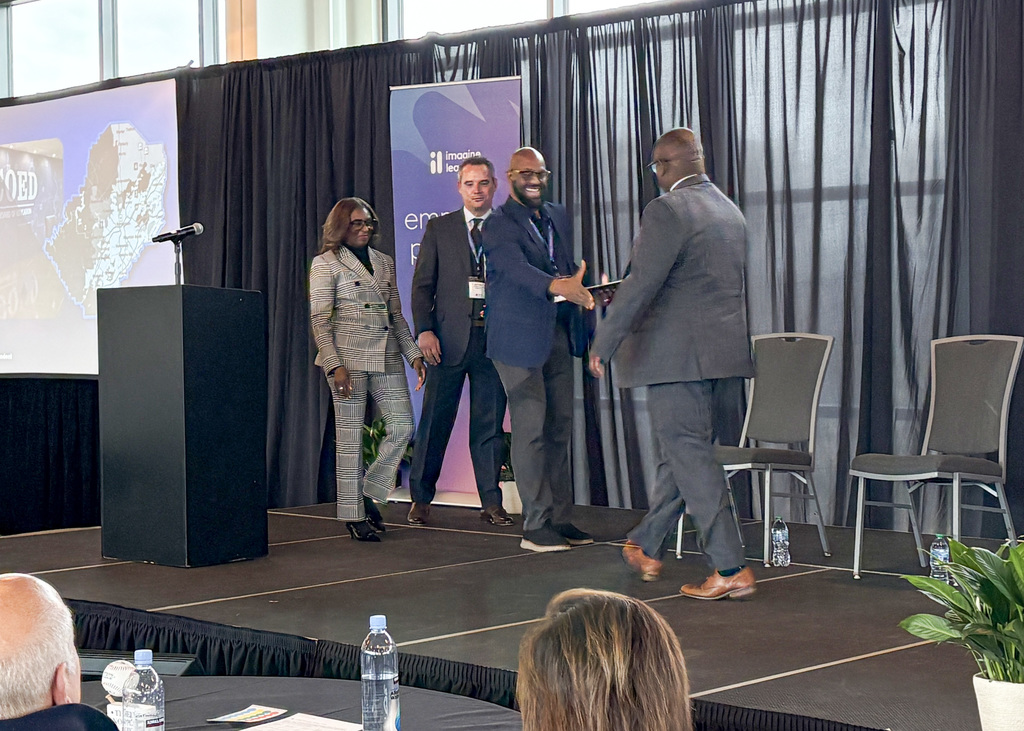 Two men greet each other on stage with a handshake. 