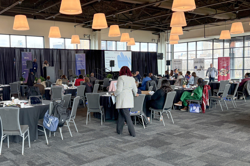 A room full of meeting attendees sitting at tables. 