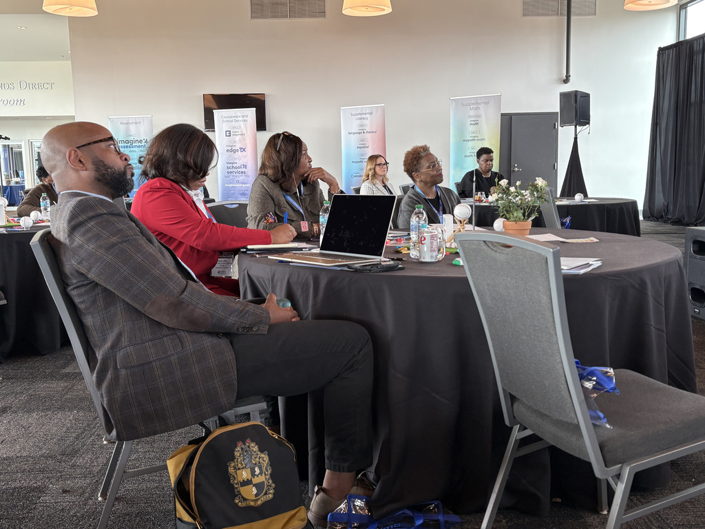 A table full of people watch a speech during a conference. 