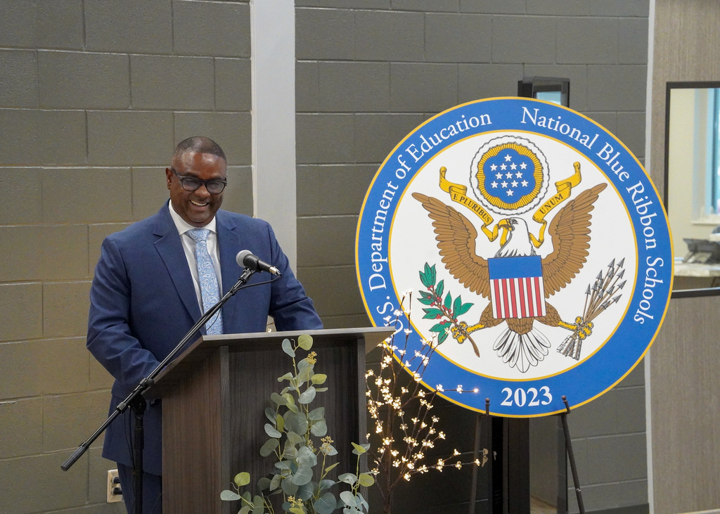 Superintendent Dr. Walter Gonsoulin smiles while standing at a podium during the ribbon cutting ceremony of the new JCIB school.