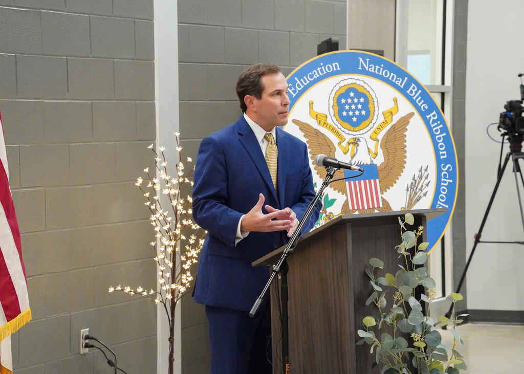 Jeff Caufield speaks into a microphone at a podium during the ribbon cutting ceremony of the new JCIB school.