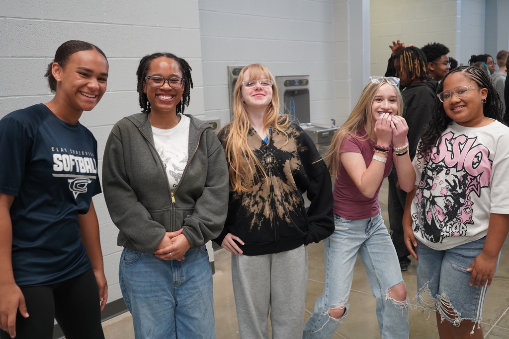 Five students smile for a photo while standing in a school hallway.