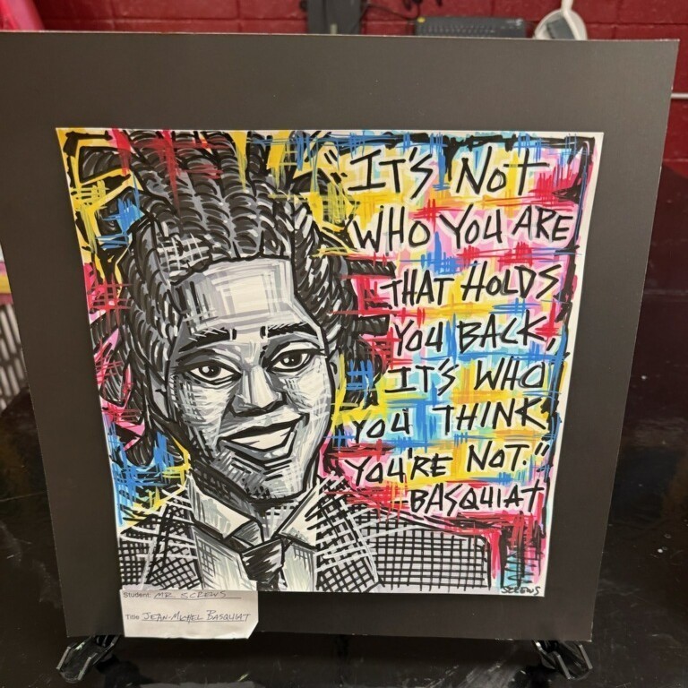 A work of student art. The art depicts an African American man. The quote on the art reads, "It's not who you are that holds you back, it's who you think you're not." Basquiat