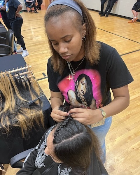 An African-American female student braids another student's hair.