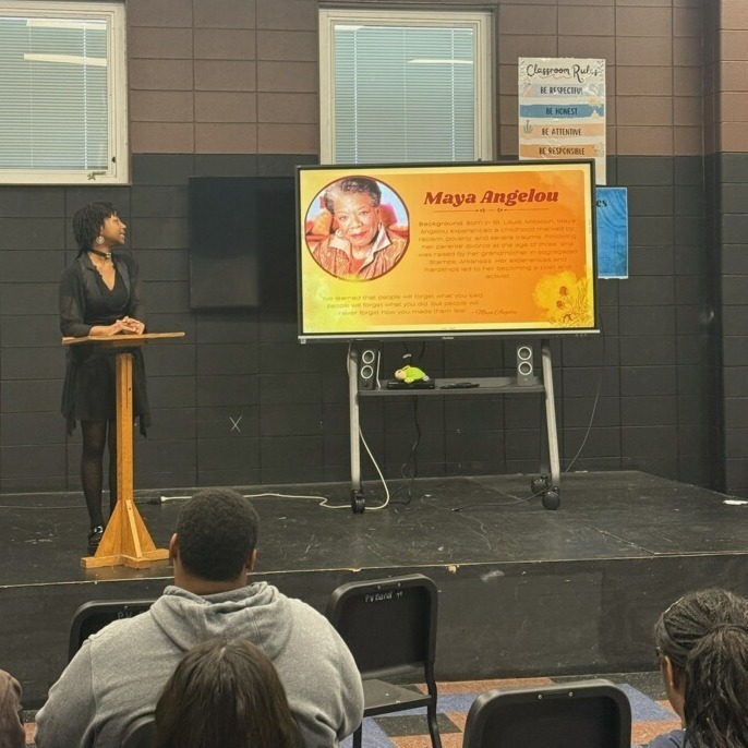 A student is standing on a small stage while making a presentation on Maya Angelou.