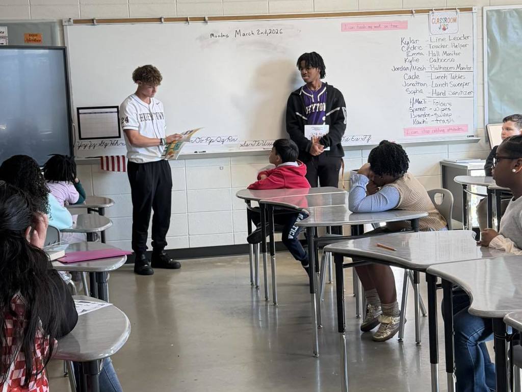 Two Hueytown High School baseball players read to students in a classroom.