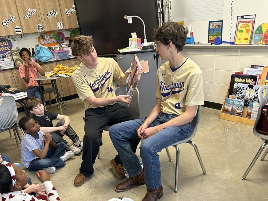 Two Hueytown High School baseball players read to students in a classroom.