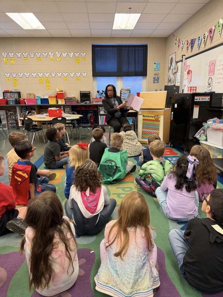 Dr. Angela Watkins reads a books to a group of students inside a classroom.