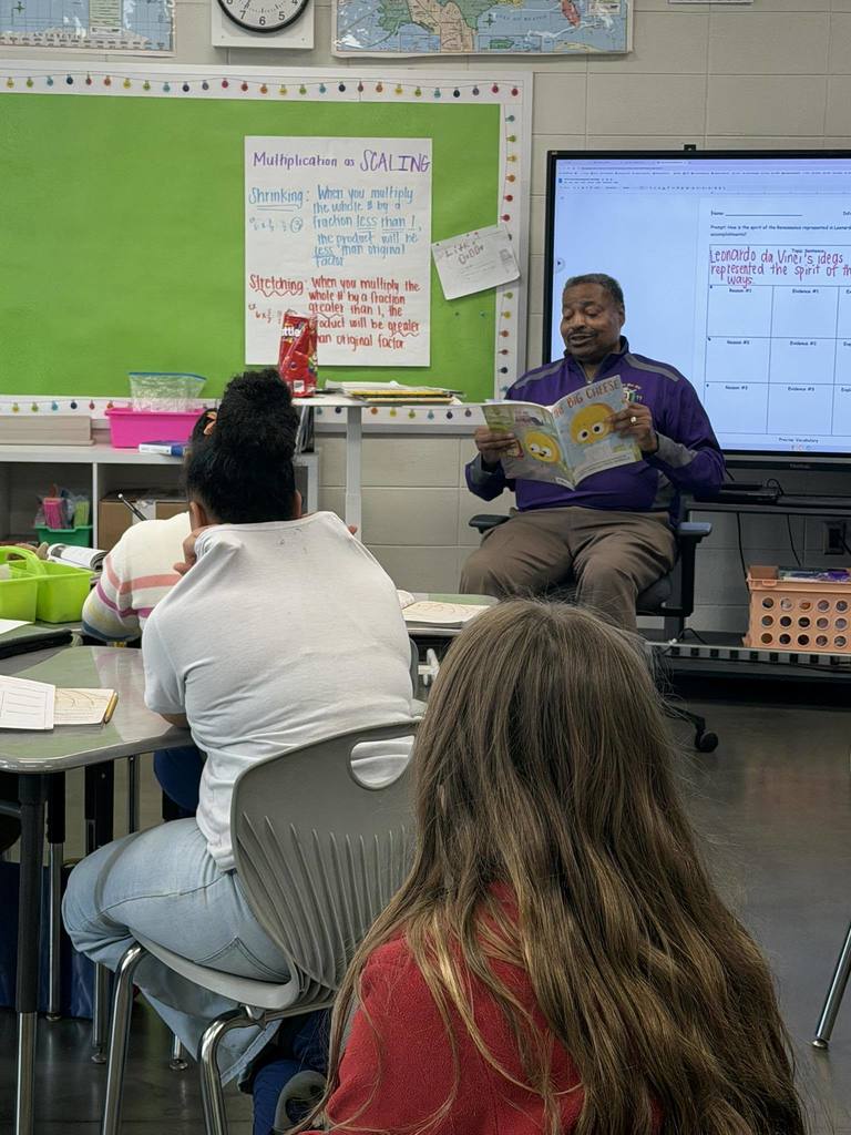 A man reads a book to a classroom of students.
