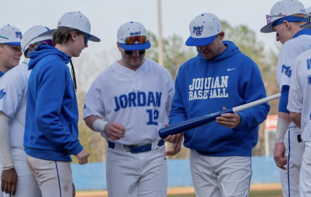 Moritmer Jordan baseball players stand on the field and present his coach with a bat to congratulate him on his 500th career win.