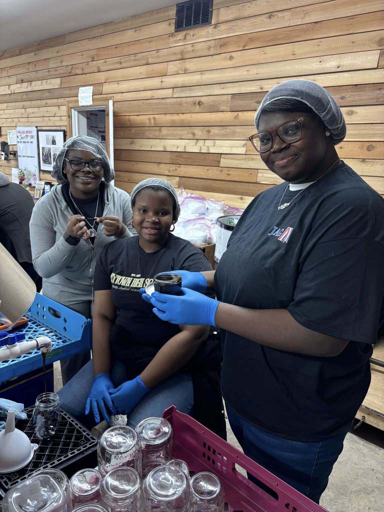 Students wearing hair nets hold jars while volunteering with Grace Klein Community.