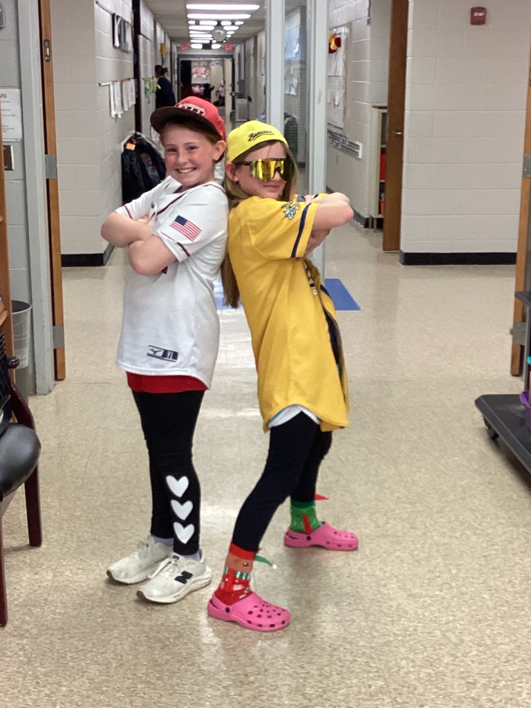 Two students are posing in front of the library doors in wacky clothes for day 3 of Read Across America week. Students clothing is mismatched.