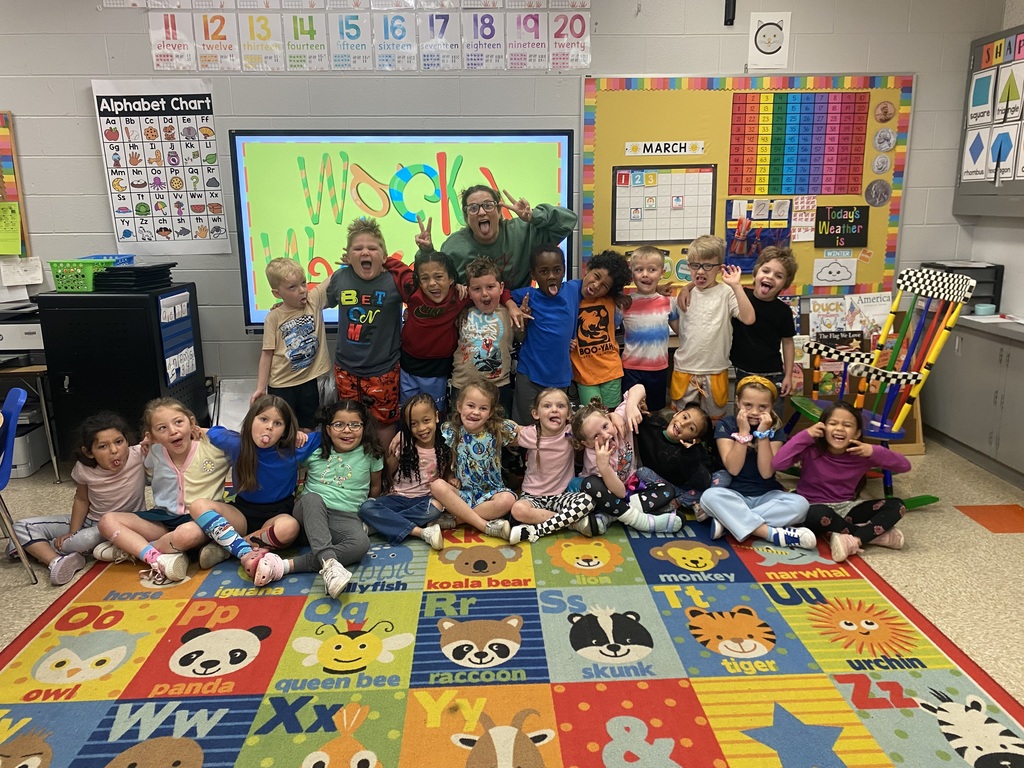 Students are showing off silly poses in front of a kindergarten whiteboard in wacky clothes for day 3 of Read Across America week. Students clothing is mismatched and inside out.