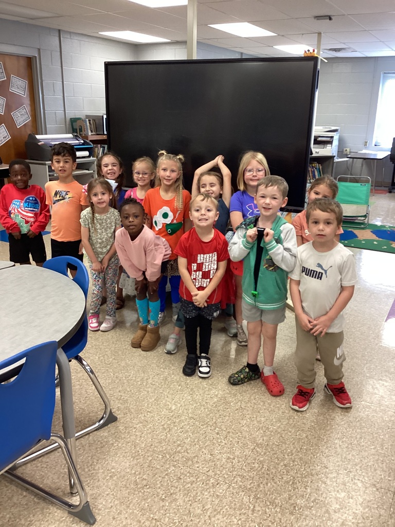 Students posing in front of the library whiteboard in wacky clothes for day 3 of Read Across America week. Students clothing is mismatched and inside out.
