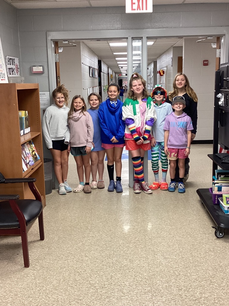 Students posing in front of the library doors in wacky clothes for day 3 of Read Across America week. Students clothing is mismatched and inside out.