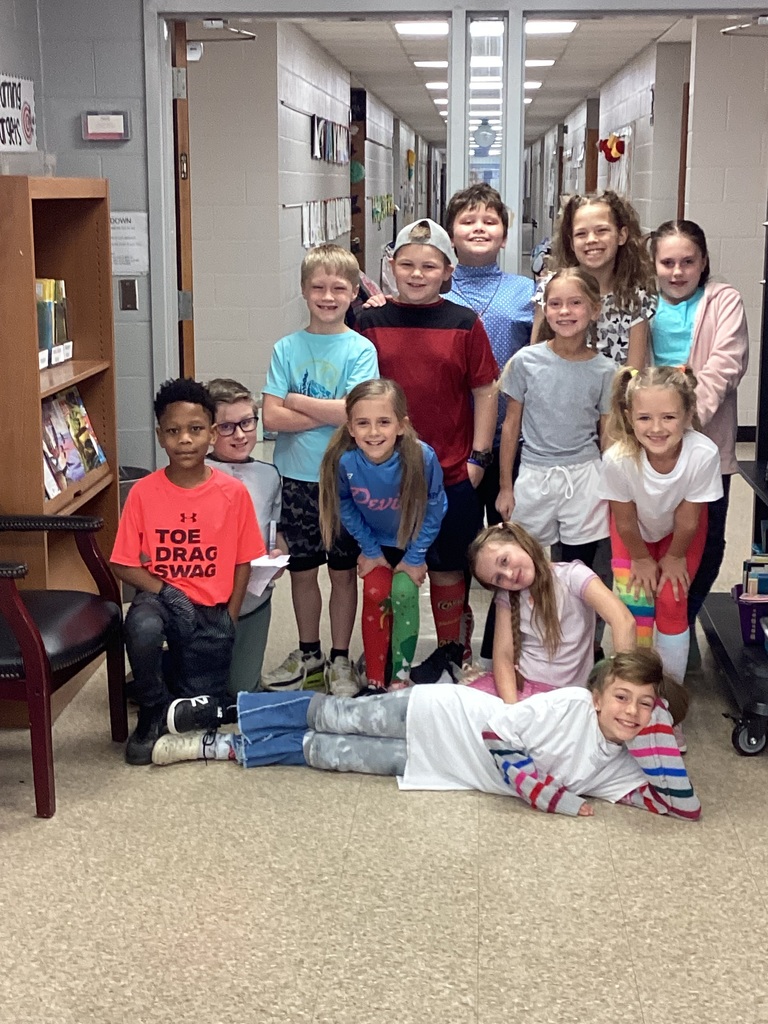 Students posing in front of the library doors in wacky clothes for day 3 of Read Across America week. Students clothing is mismatched and inside out.