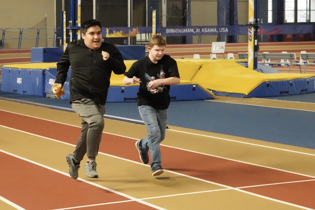 Two students run next to each other as they race down the track at the Birmingham CrossPlex.
