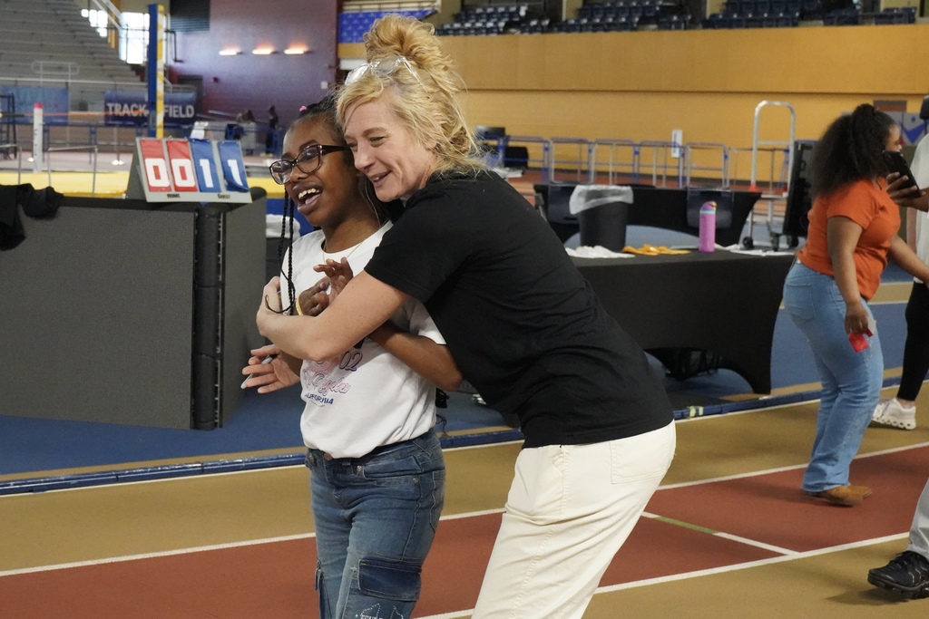 A child smiles as an adult hugs her. They stand on the track at the Birmingham CrossPlex.
