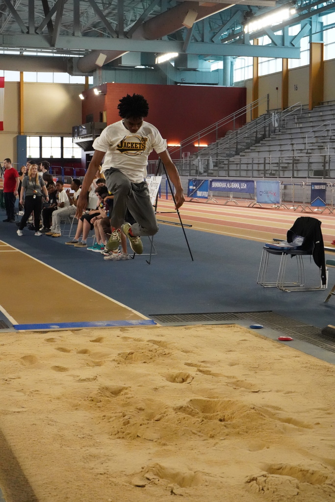 A student jumps into a sand pit while at the track at the Birmingham CrossPlex.