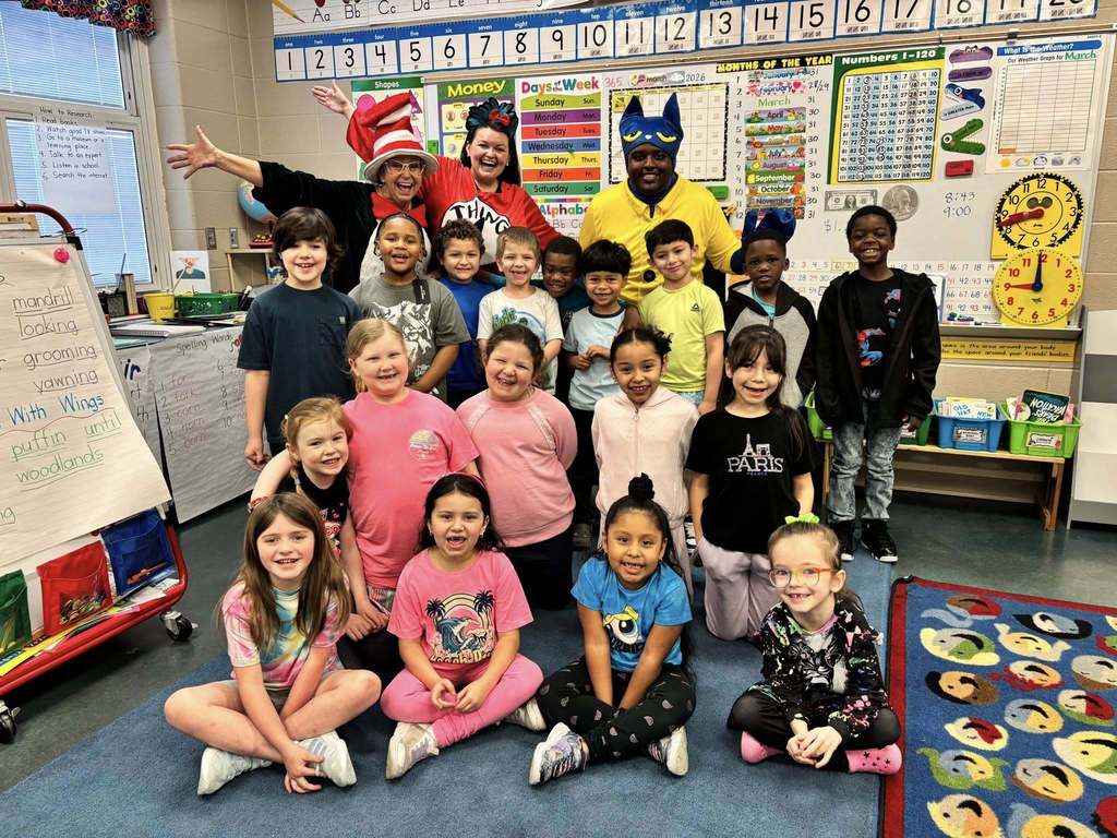 Students and educators pose for a photo inside a classroom. The educators wear costumes to celebrate Read Across America Week.