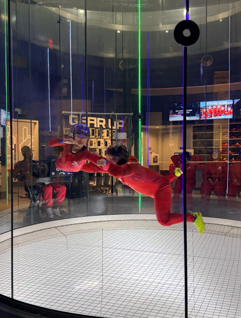 An instructor holds a participant during an indoor skydiving lesson. Both are floating in the air.