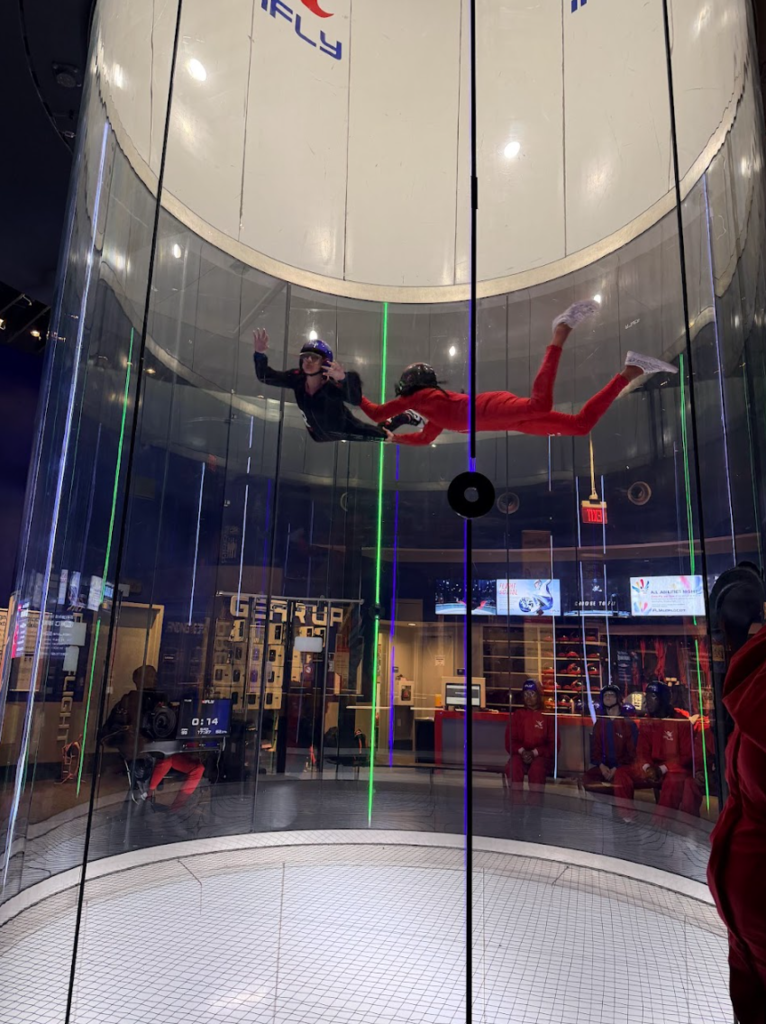 An instructor and participant soar through the air during an indoor skydiving lesson.