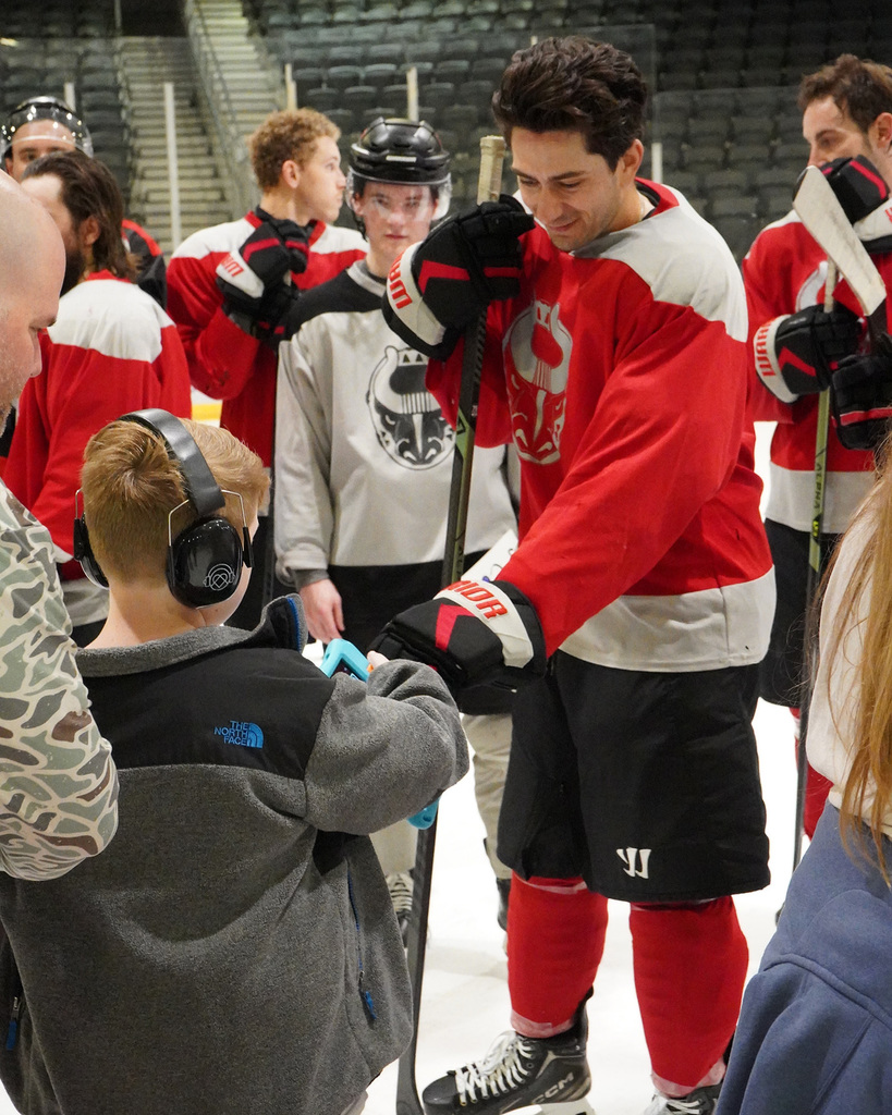 A member of the Birmingham Bulls hockey team is giving a fist bump to a student wearing headphones. Other hockey players are in the background.