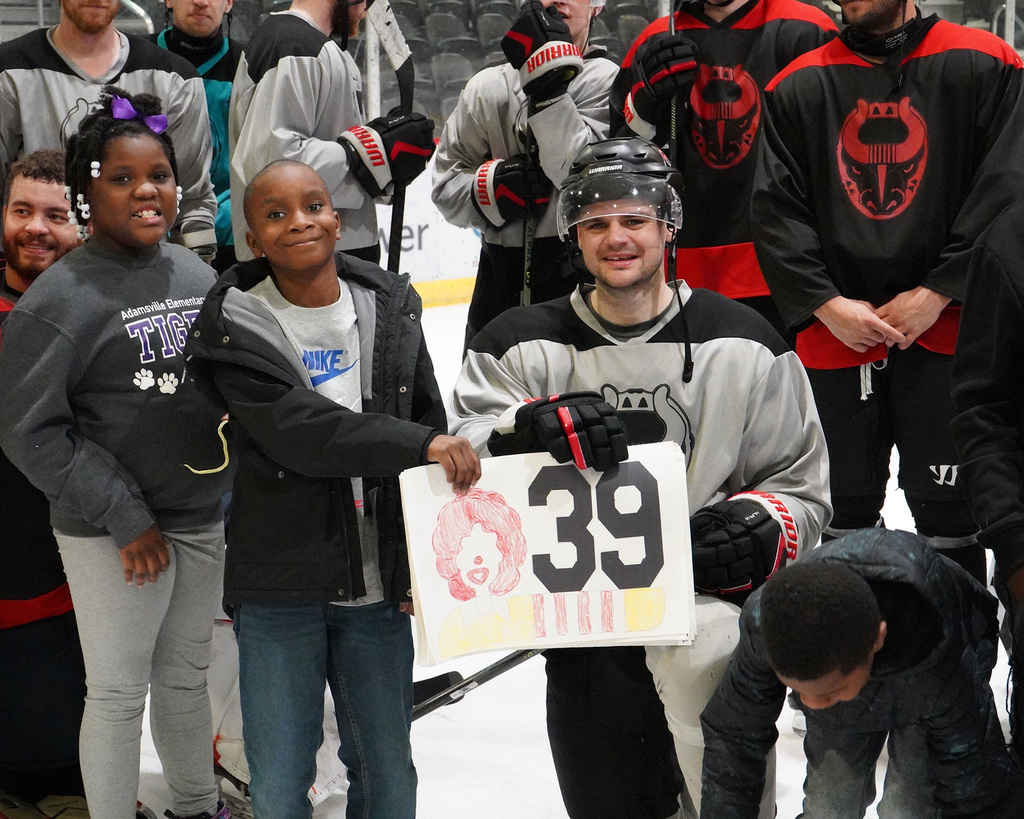 Two students and a hockey player are holding up a sign the students made for the player. All are smiling.