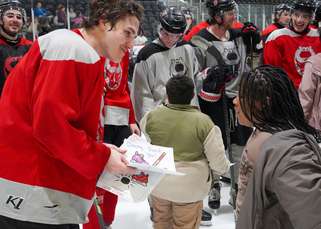 An elementary school student gives a smiling Birmingham Bulls hockey player a sign.