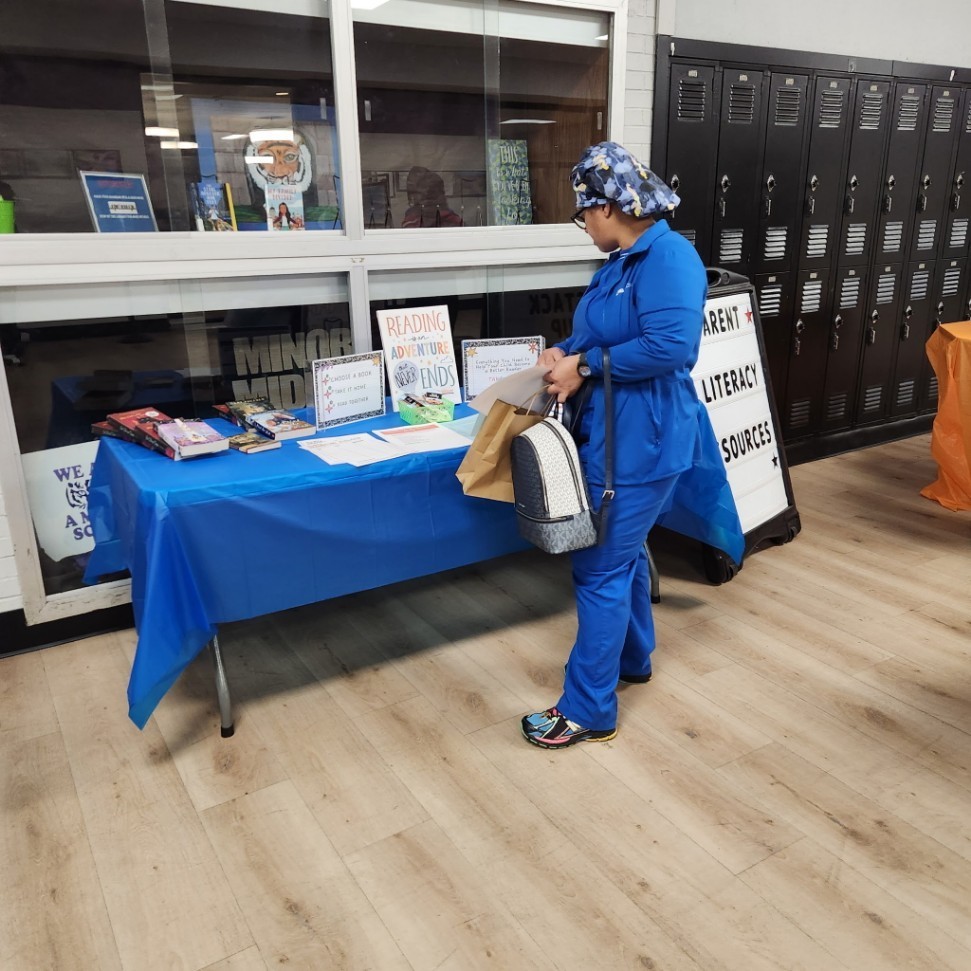 A parent in scrubs. While attending the Parent Night, stopped by the literacy sources table to gather materials to support her student's learning at home.