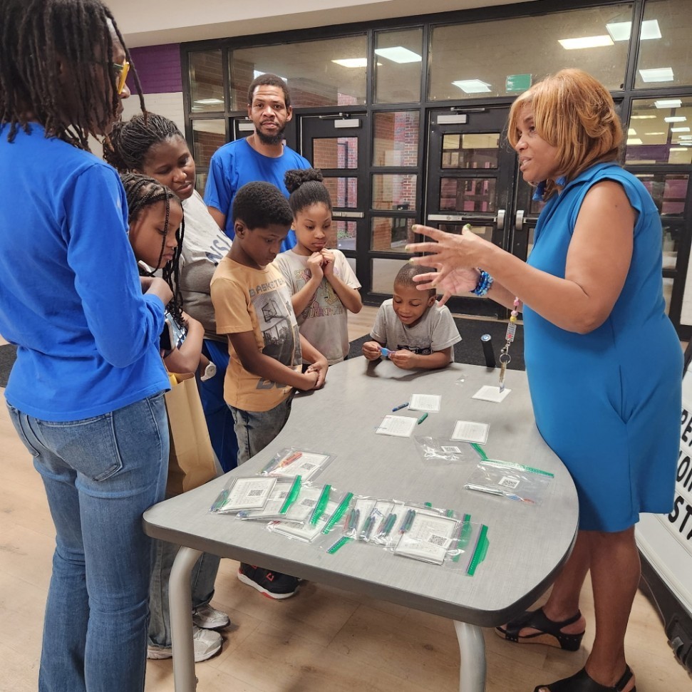 Ms. Clark answering questions and explaining the Product Game to Parents who stopped by her table during Parent Night.