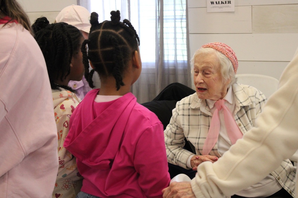 A woman talks to two little girls while they sit and stand inside a room.