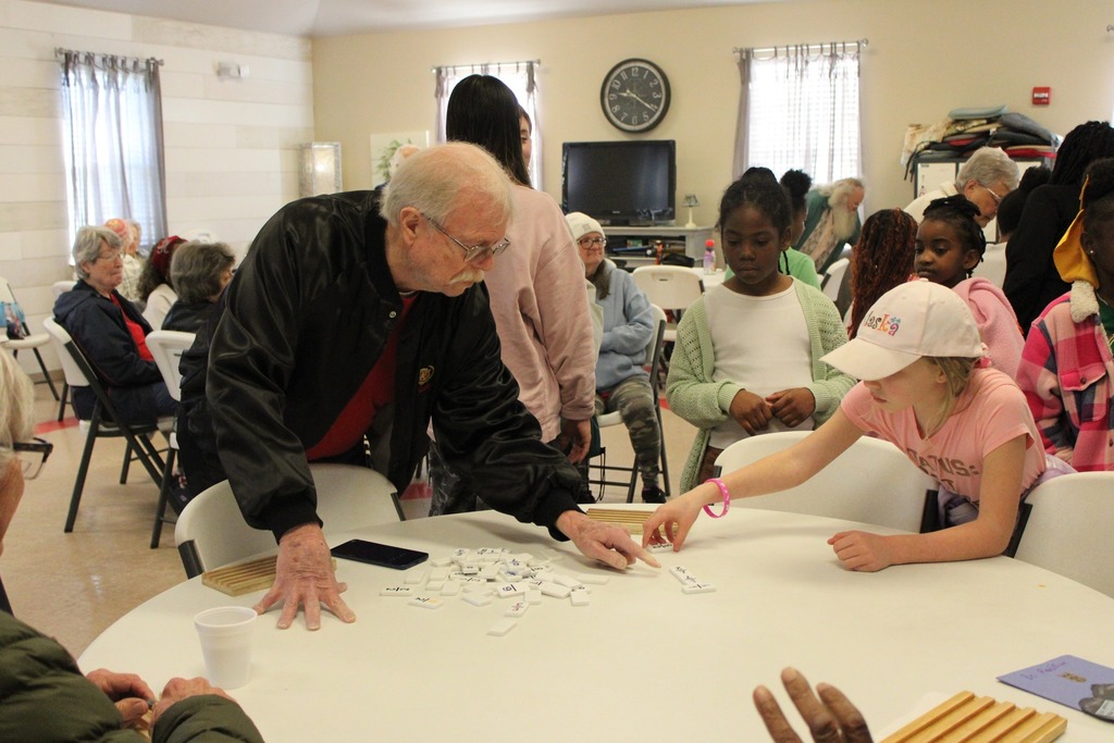A man shows a group of students how to play a game inside a senior center.