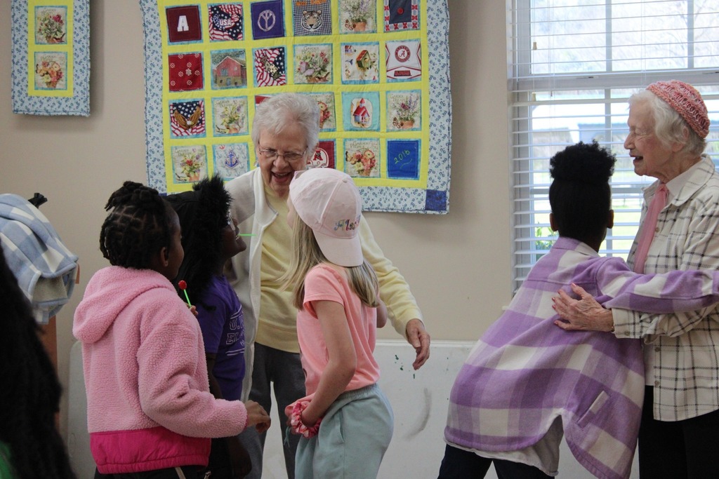 A group of girls hug women inside a senior center.