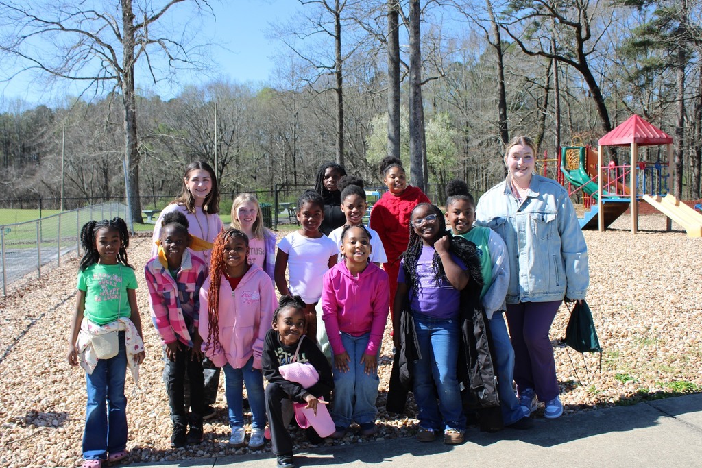 A group of students and educators stand together and smile for a photo. They stand outside at a playground.