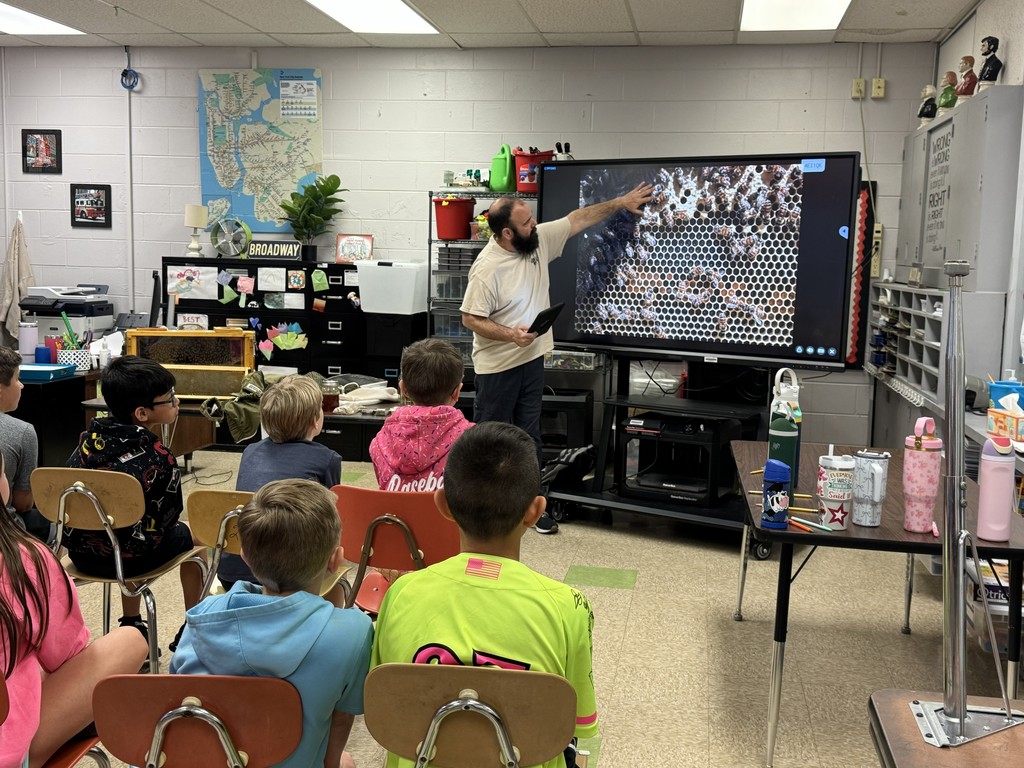A visiting beekeeper points to an enlarged photo of a hive on an interactive whiteboard. 
