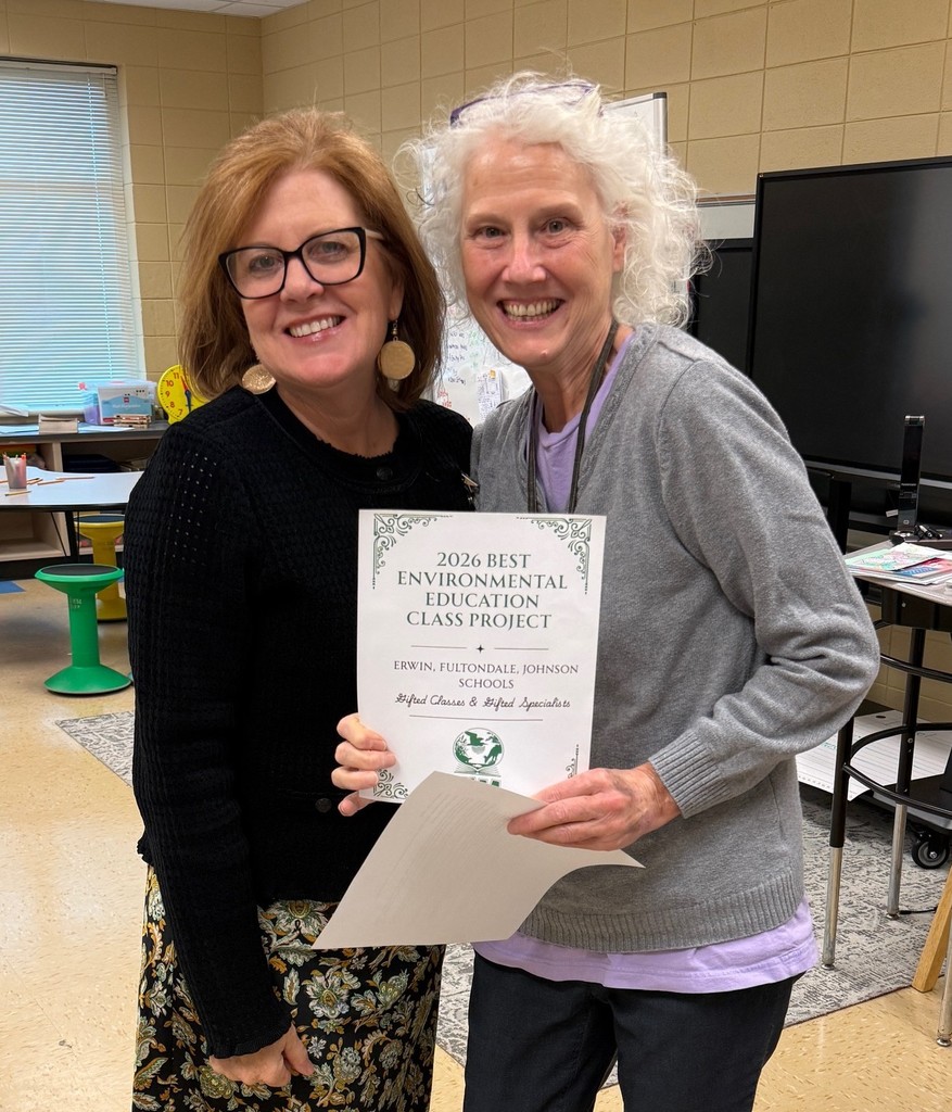 Two women stand together for a photo inside a classroom and smile. The woman on the right side of the photo holds a paper that says "2026 Best Environmental Education Class Project," followed by the schools that received the award. The schools include Erwin, Fultondale and Johnson Elementary Schools.