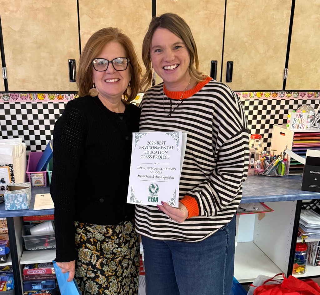 Two women stand together for a photo inside a room and smile. The woman on the right side of the photo holds a paper that says "2026 Best Environmental Education Class Project," followed by the schools that received the award. The schools include Erwin, Fultondale and Johnson Elementary Schools.